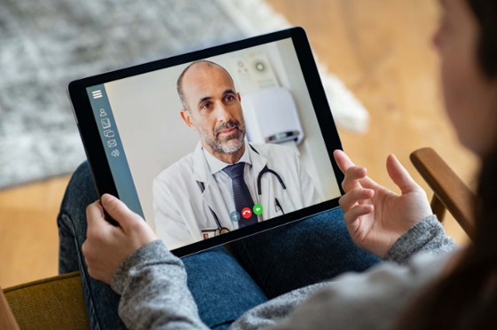 Photo of a patient holding a tablet with a video call open, speaking to a medical professional.