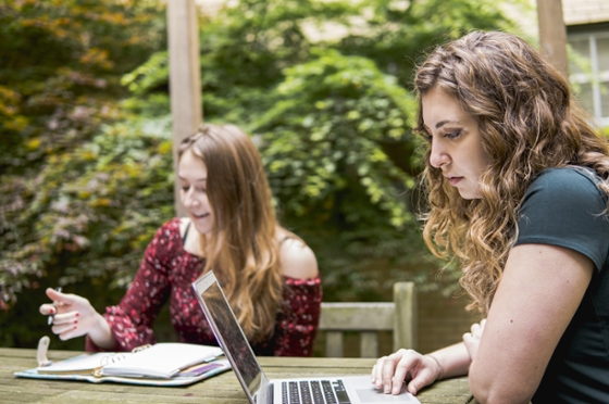 Two Chatham University students sit outside at a bistro table studying independently on their laptops. 