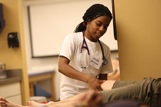 Photo of a Chatham University student assisting a patient who is laying down on a table