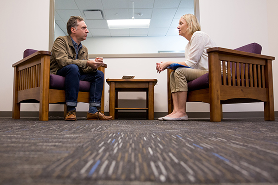 Photo of a man and a woman sitting across from each other in chairs during a counseling session