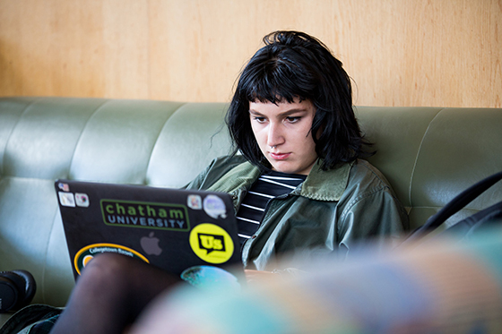 Photo of a Chatham University student sitting on a green couch, working on a computer