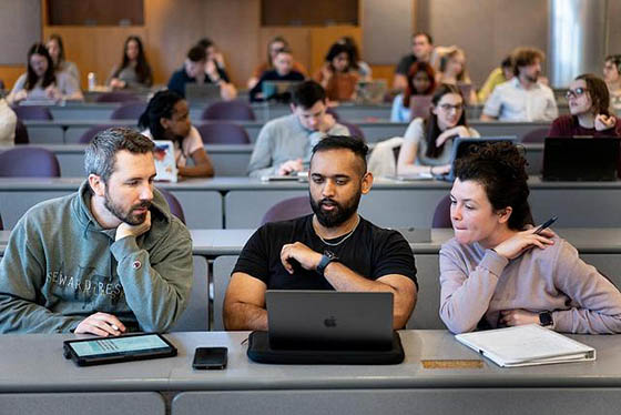 Photo of a male Chatham University student seated next to classmates, paying attention to an unseen lecturer
