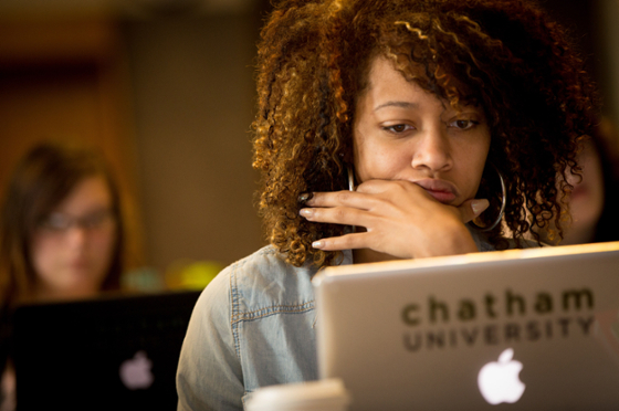 Photo of a student taking notes on a laptop with Chatham University sticker during a lecture. 