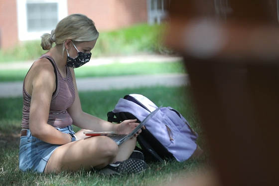 Photo of a masked female Chatham University student working on her laptop outside on Shadyside Campus