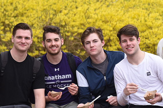 Photo of four male Chatham University students posing together outside smiling and eating ice cream