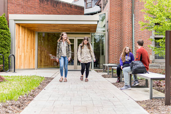 Photo of two Chatham University students walking on Shadyside Campus, with two other students seated nearby on a bench