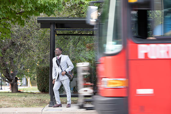 Photo of a man waiting for a bus, with a blurred bus passing into the frame