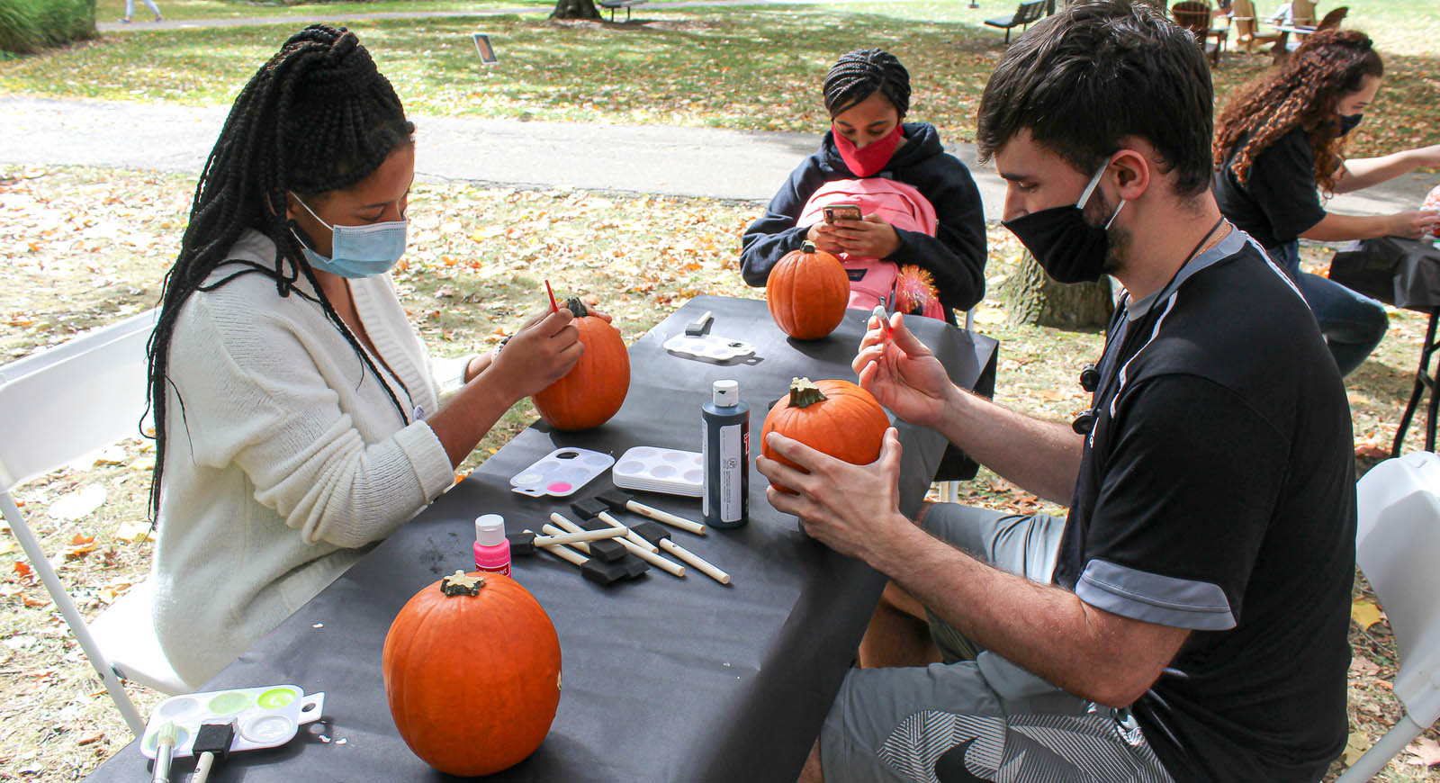 Photo of students painting pumpkins at a picnic table on the quad