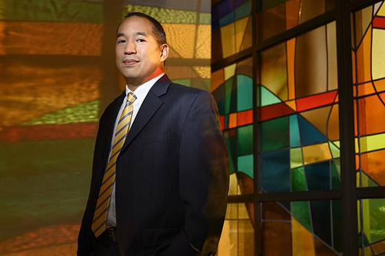 Portrait of an Asian businessman in a suit, standing in front of a brightly colored art display