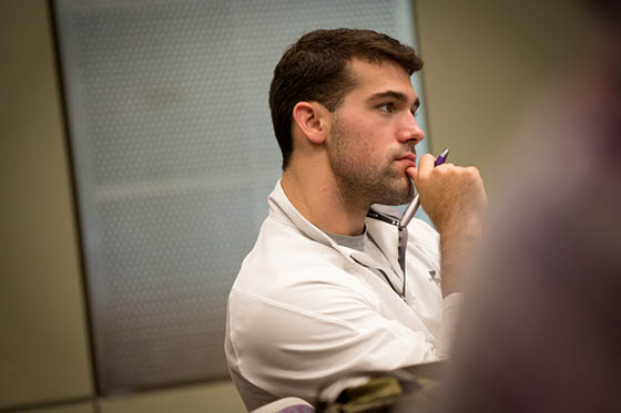 Photo of student in a white polo shirt, sitting with his hand to his chin paying attention to a lecture