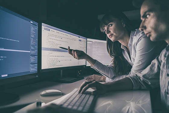 Photo of a man and a woman leaning over a computer monitor in a dark room.