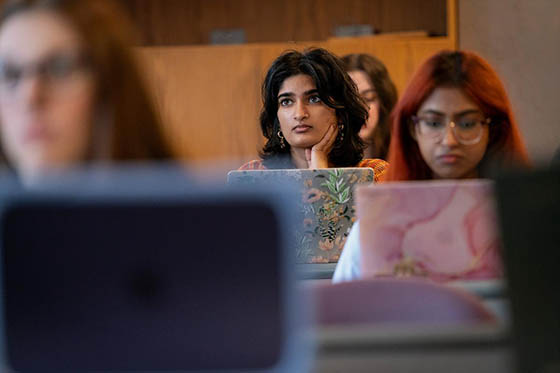 Photo of a female Chatham University student standing in front of her presentation, as two professors offer thoughts.