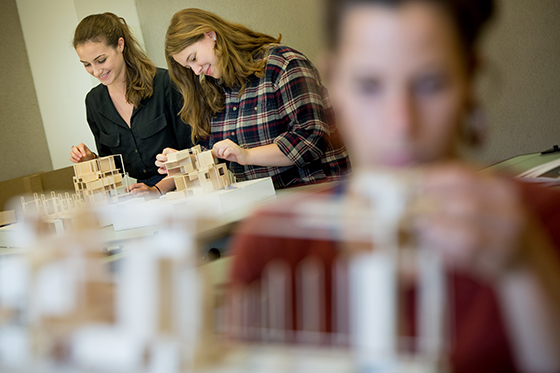 Photo of two Chatham University students working in an architecture lab building models with wood.