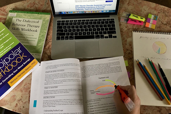 Photo from above of a student highlighting a diagram in a psychology notebook on a table filled with psychology notebooks, pens, and a laptop. 