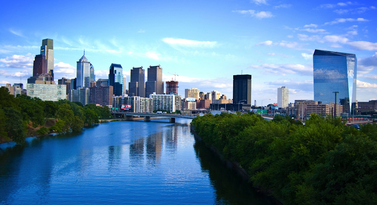 Photo of the Philadelphia skyline with a river and blue sky. 