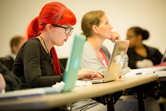 Photo of a Chatham University student with bright red hair working on her laptop in a lecture hall