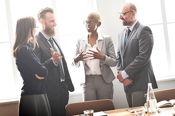 Photo of a group of four business professionals speaking in a well-lit conference room.