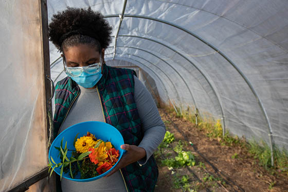 Photo of a female Chatham University student holding a bowl of harvested produce at the door of a greenhouse on Eden Hall Campus