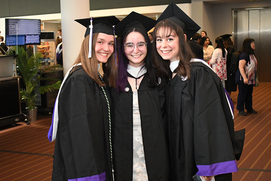 Photo of three young Chatham University female students in graduation robes and caps posing for a photo