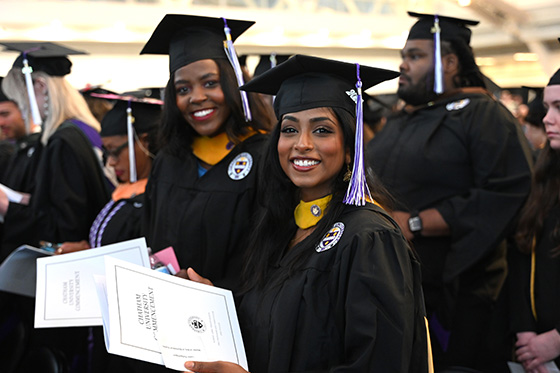 Two Chatham University graduates in gowns and caps pose for a photo