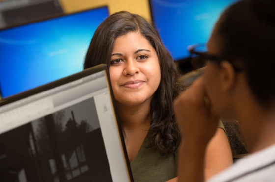 Photo of a Chatham University student in a computer lab talking to a student behind her.
