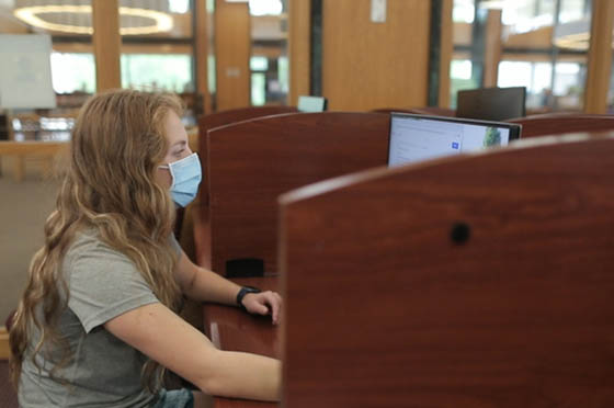 Photo of a female Chatham University student wearing a mask, working on a computer in the library
