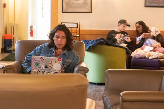 Students sit in the Carriage House, working on laptops and talking together