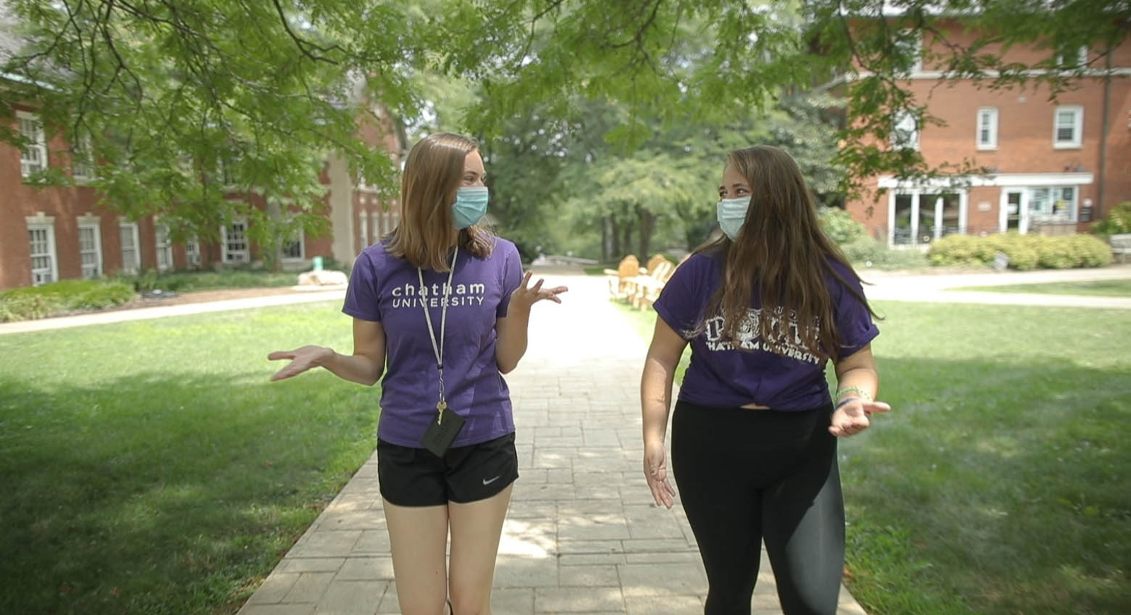 Photo of two female Chatham University students with masks on, walking on Shadyside Campus and speaking to one another