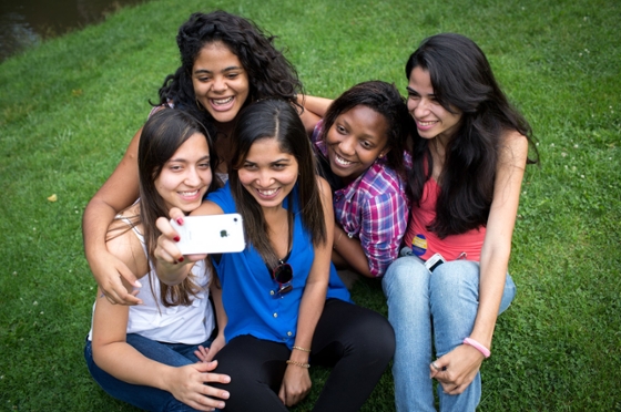 Photo of a group of five young women taking a selfie while seated outside in the grass