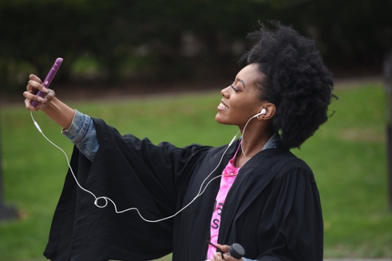 Photo of a female Chatham University student in graduation robes, taking a selfie and smiling