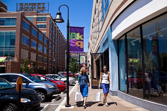 Photo of two women walking down a sidewalk in Bakery Square, Pittsburgh holding shopping bags and passing storefronts. 
