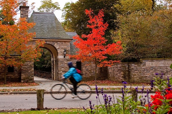 Photo of a bicyclist passing stone entrance to Frick Park in Pittsburgh framed by colorful fall foliage. 
