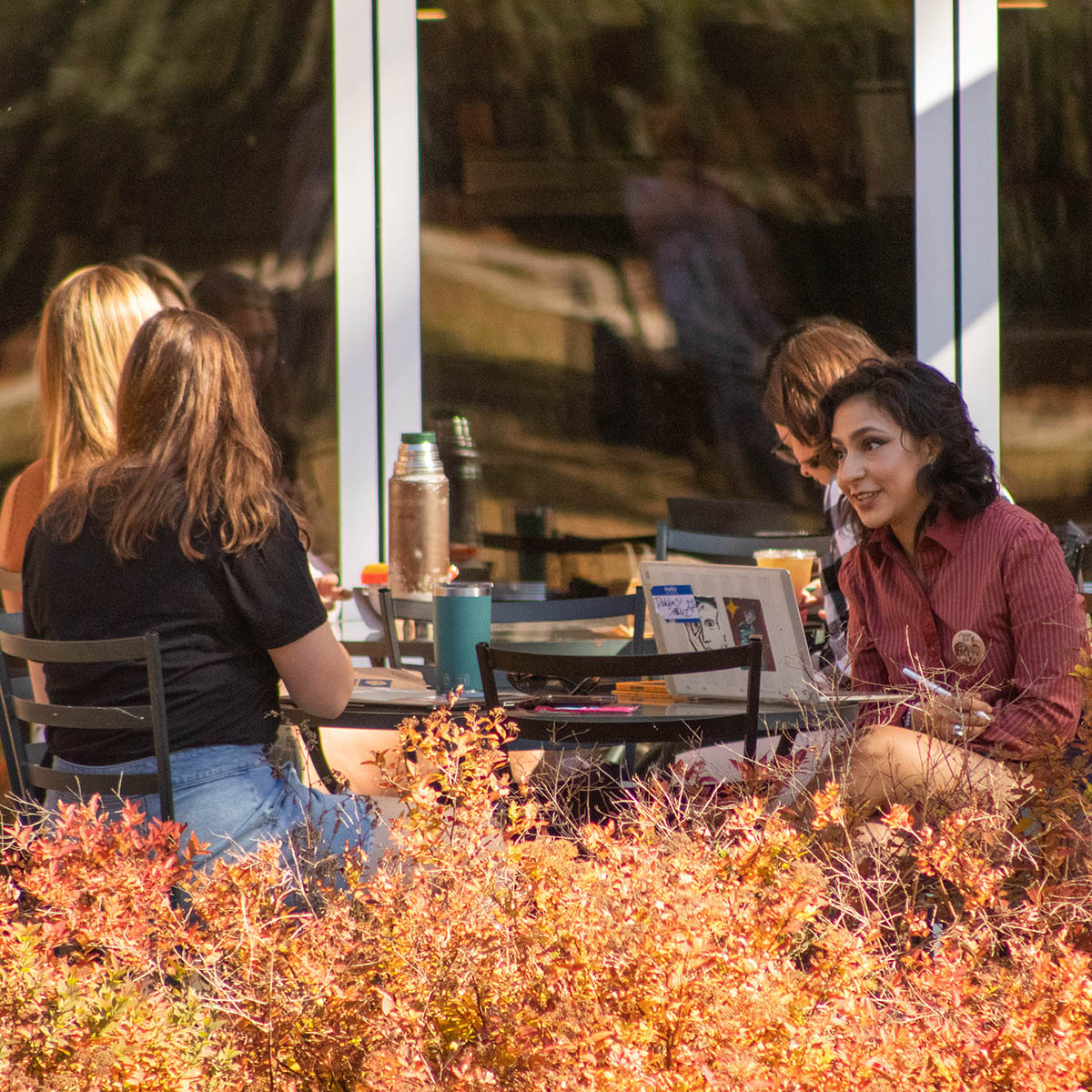 Photo of students seated at Cafe Rachel tables outdoors, with autumn foliage in the foreground