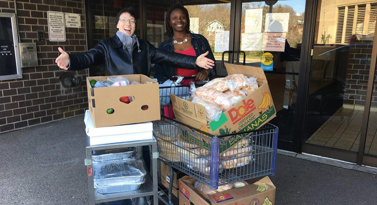 Photo of two smiling women standing behind shopping carts of donated food. 
