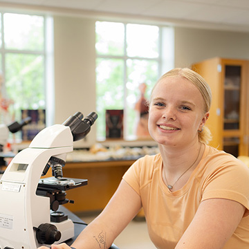 Chatham Biology student in a lab by a microscope