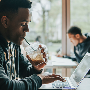 Chatham student works on laptop and drinks coffee in Café Rachel