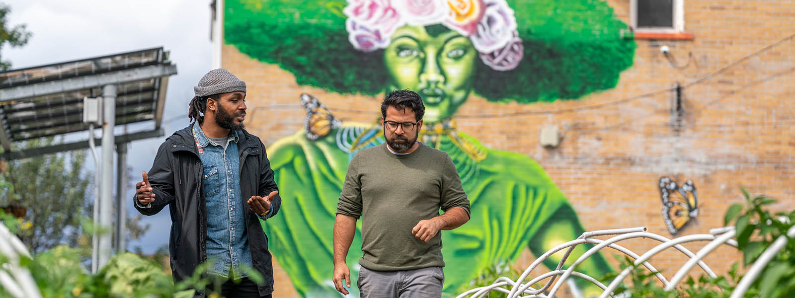 Two men walk through a community garden in an urban environment