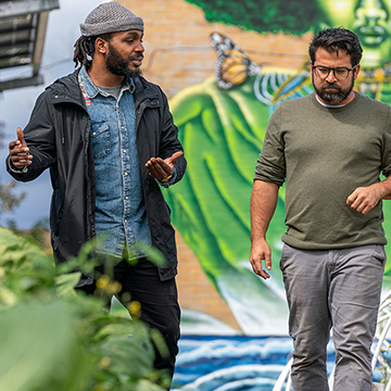 Two men walk through a community garden in an urban environment
