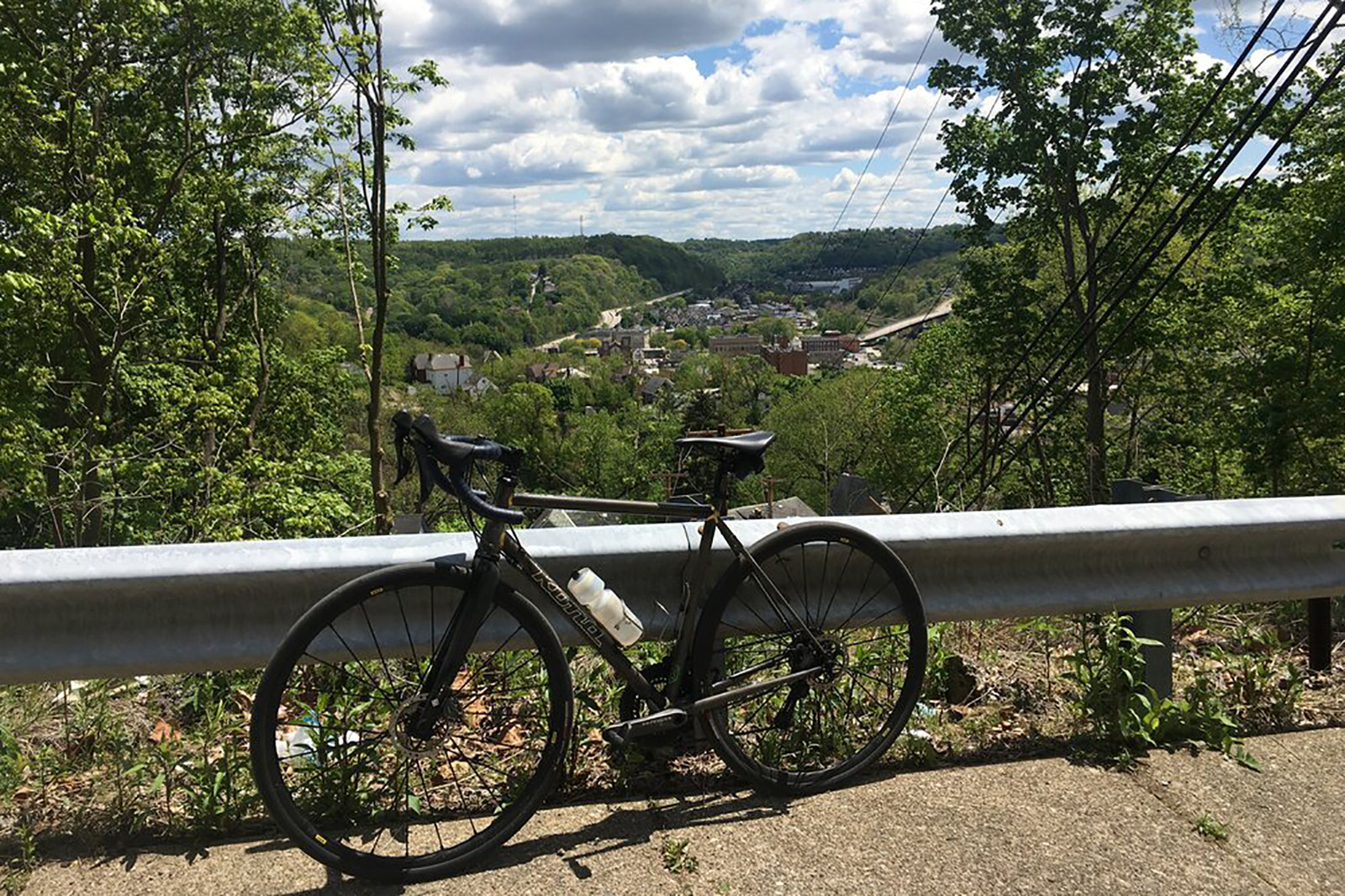 Photo of a bike leaning against a guardrail, with a view of Pittsburgh hills in the background