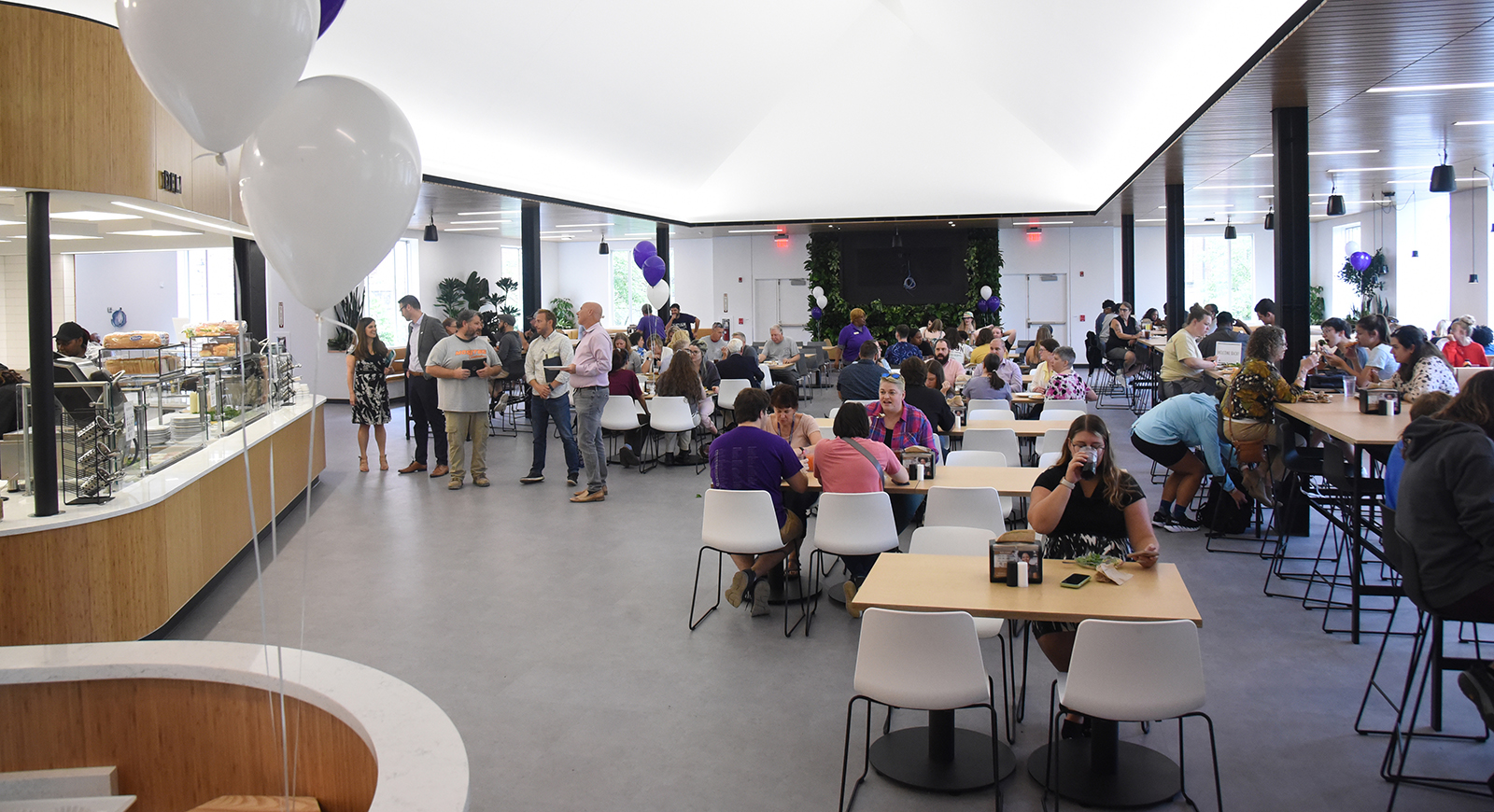 Photo of a crowded Anderson Dining Hall on opening day, with people eating and talking. There are many purple balloons.