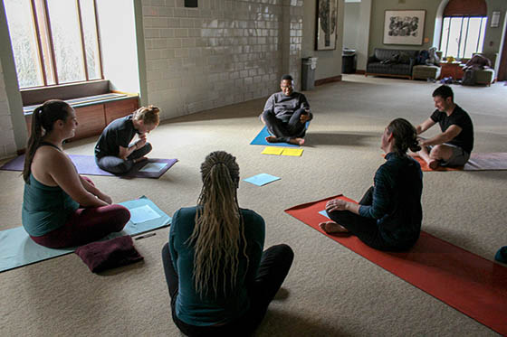 Photo of people sitting in a circle on yoga mats, in a group meditation.
